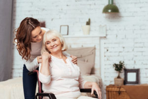 My dear. Pleasant elderly woman smiling and sitting in the wheelchair while her loving granddaughter taking care of her